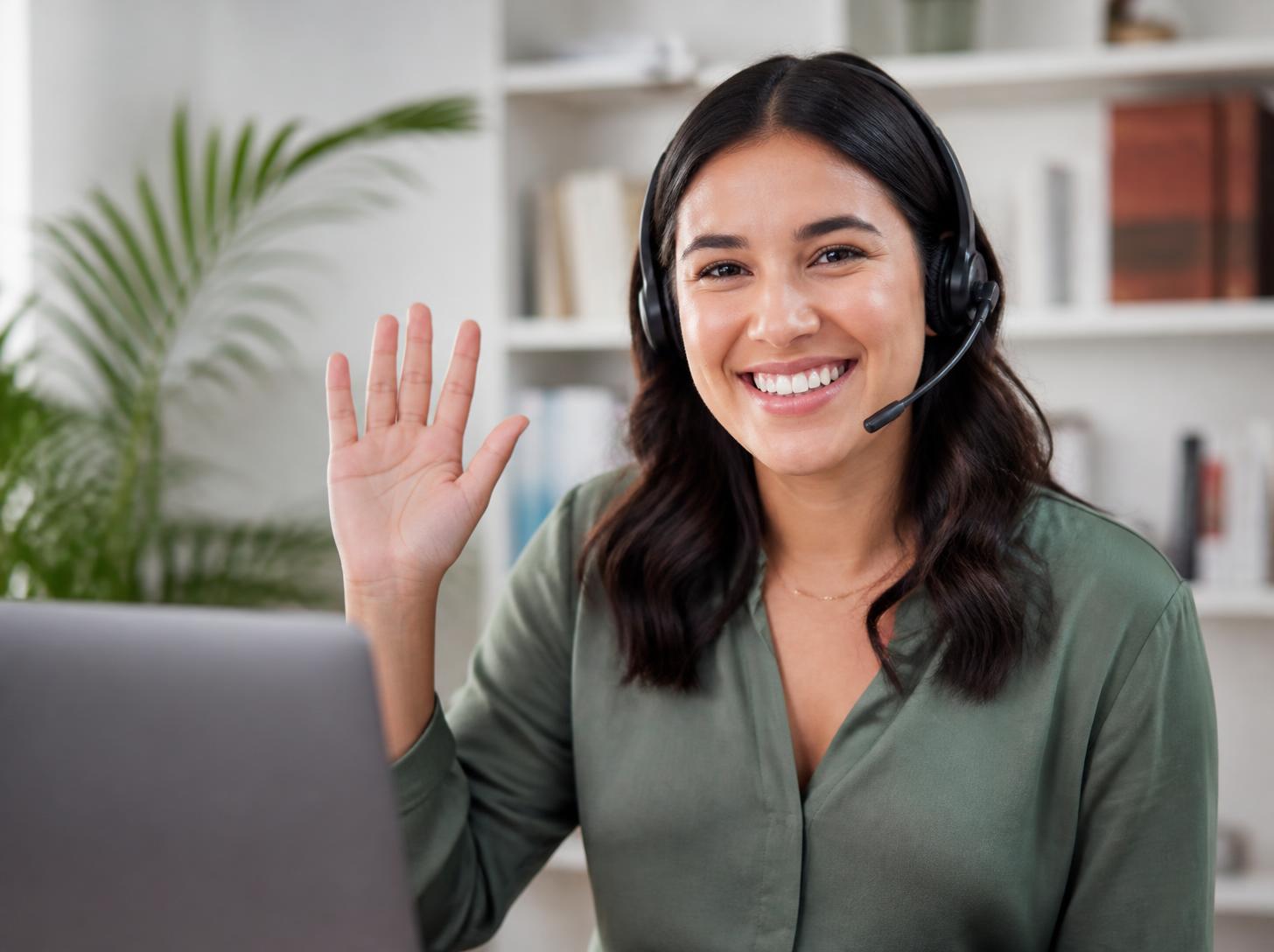 Atendente sorridente com headset acenando para a câmera, pronta para atender